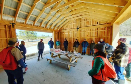 People gathered inside a wooden pavilion around a picnic table.